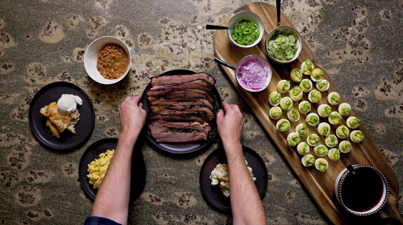 Hands setting down a platter of sliced brisket surrounded by sides